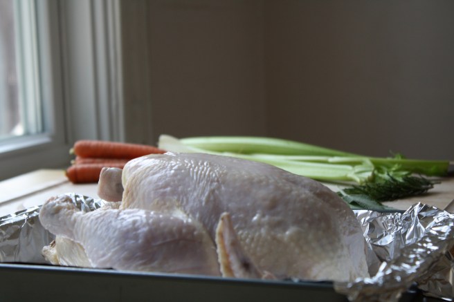A raw chicken and some raw vegetables and herbs